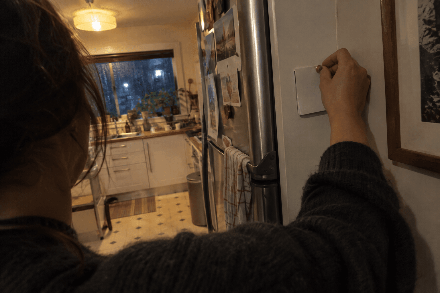 A reminder note being pinned beside a kitchen fridge.