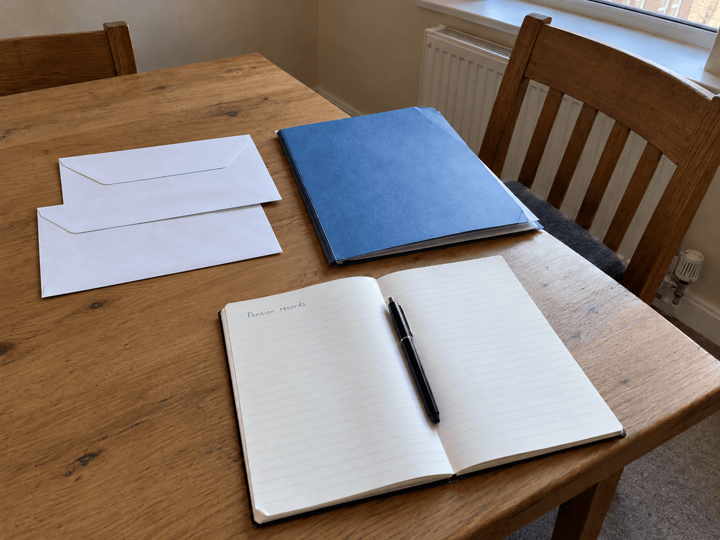 Un dossier bleu, des enveloppes et un cahier ouvert pour les documents de pension sur une table.
