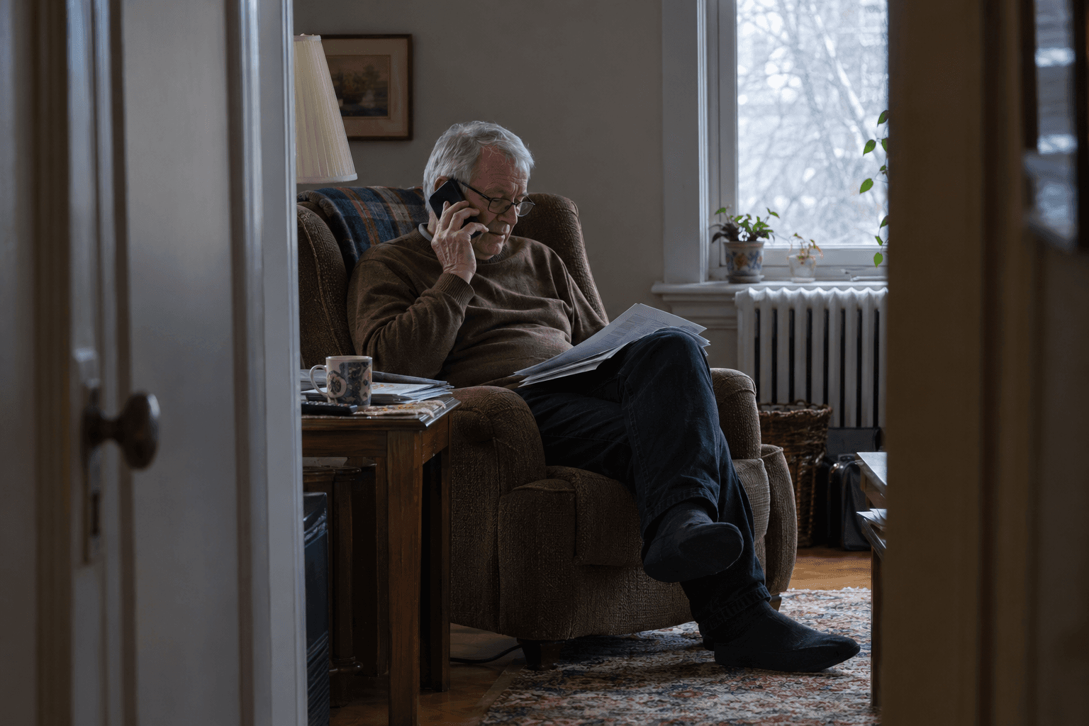 Un retraité téléphone avec ses documents de pension sur les genoux.