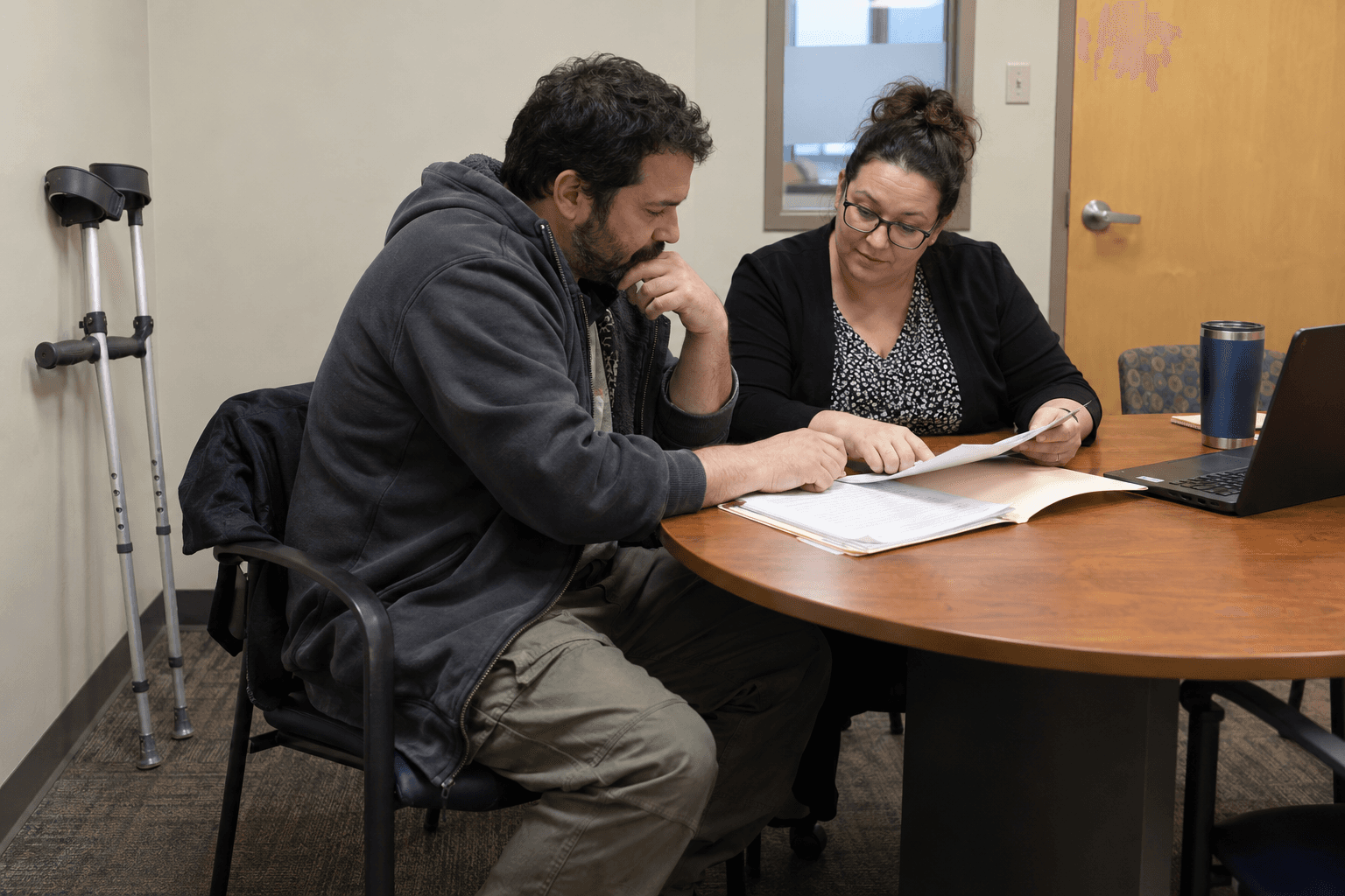 Two people reviewing a savings-plan folder at a credit-union desk.